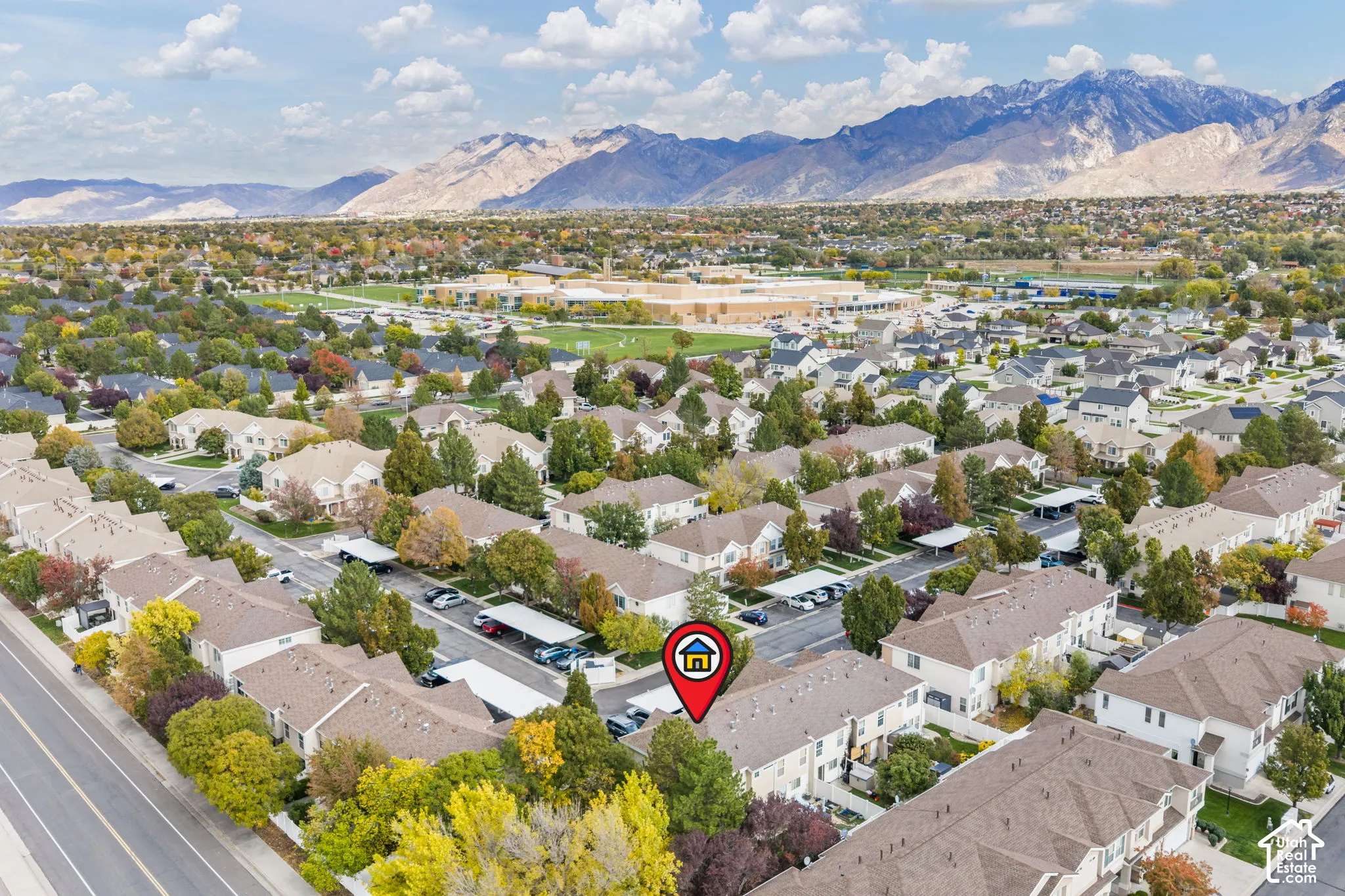 Aerial perspective of a multi-unit residential community featuring mature trees, covered parking structures, and a prominent mountain range backdrop