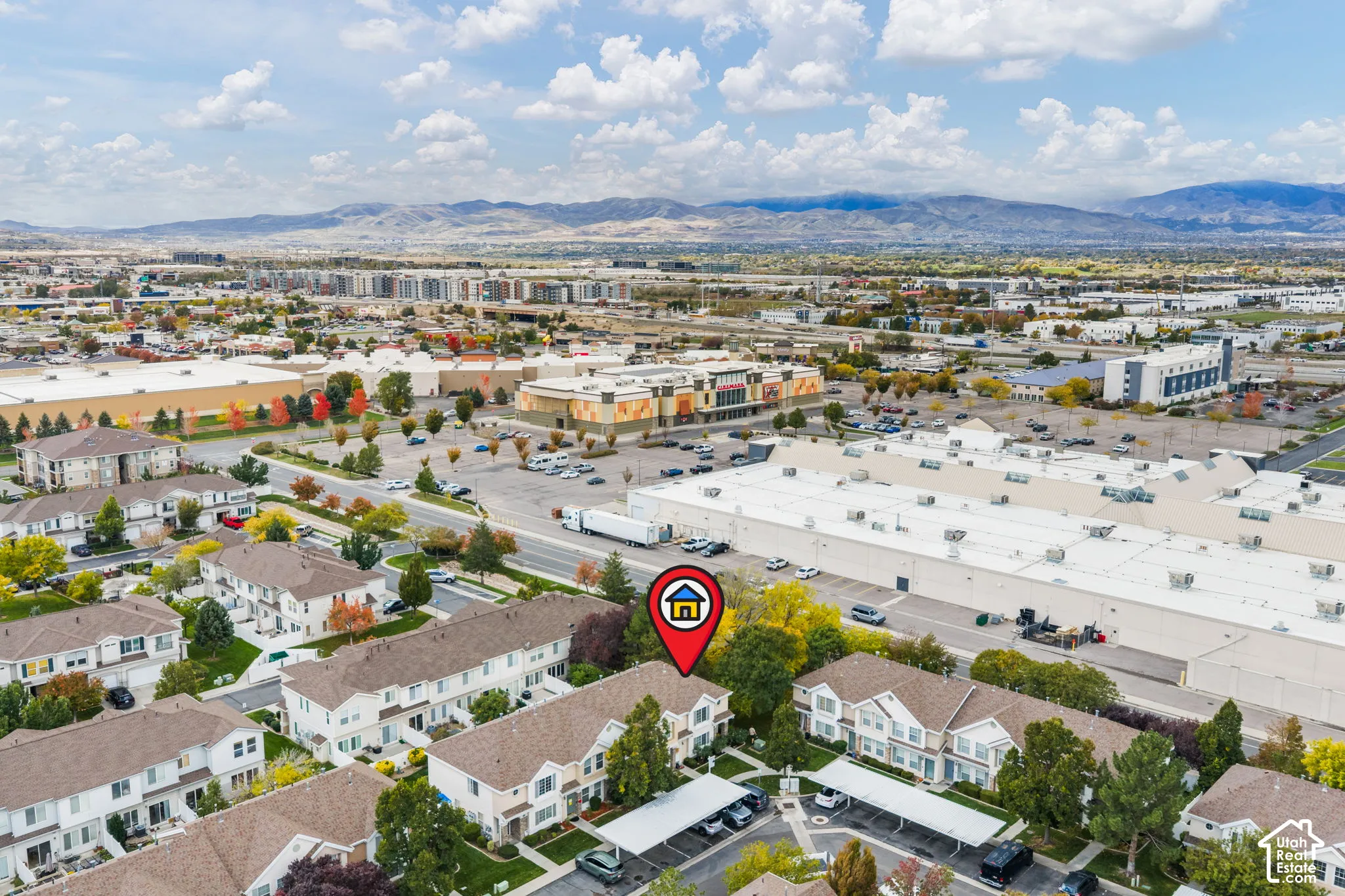 Aerial perspective featuring multi-story residential buildings with shingled roofs, covered parking structures, and mountain backdrop