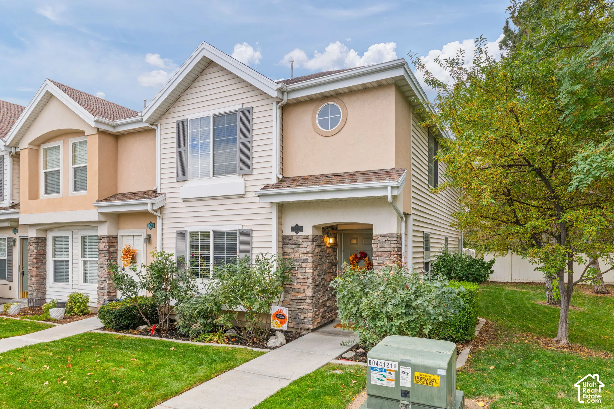 Two-story exterior featuring tan horizontal siding, stone veneer accents, multi-gabled roofline, and a circular accent window