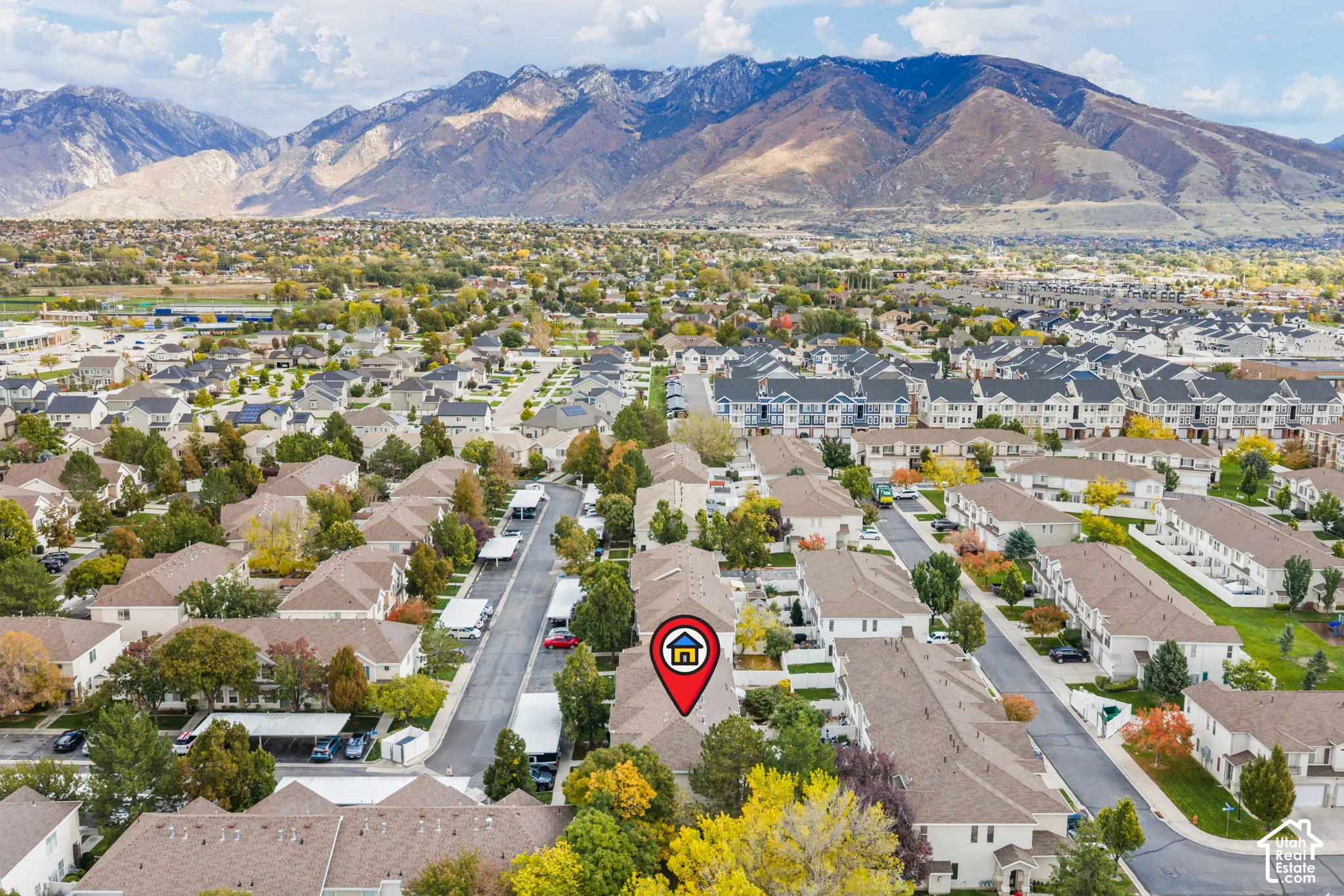 Aerial perspective featuring a residential property situated against a prominent mountain backdrop with mature trees and paved street access