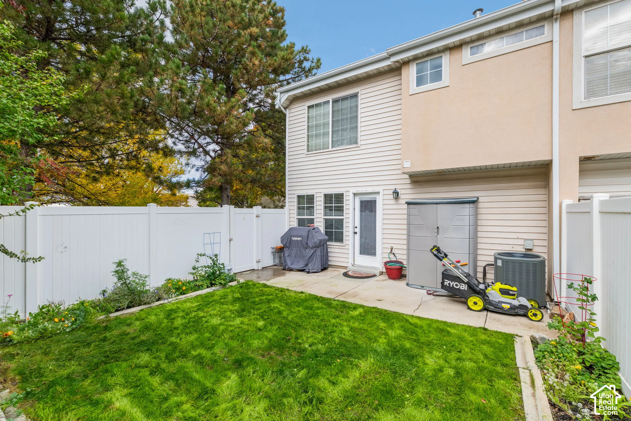 Rear exterior featuring a concrete patio, white vinyl privacy fencing, and a grass lawn