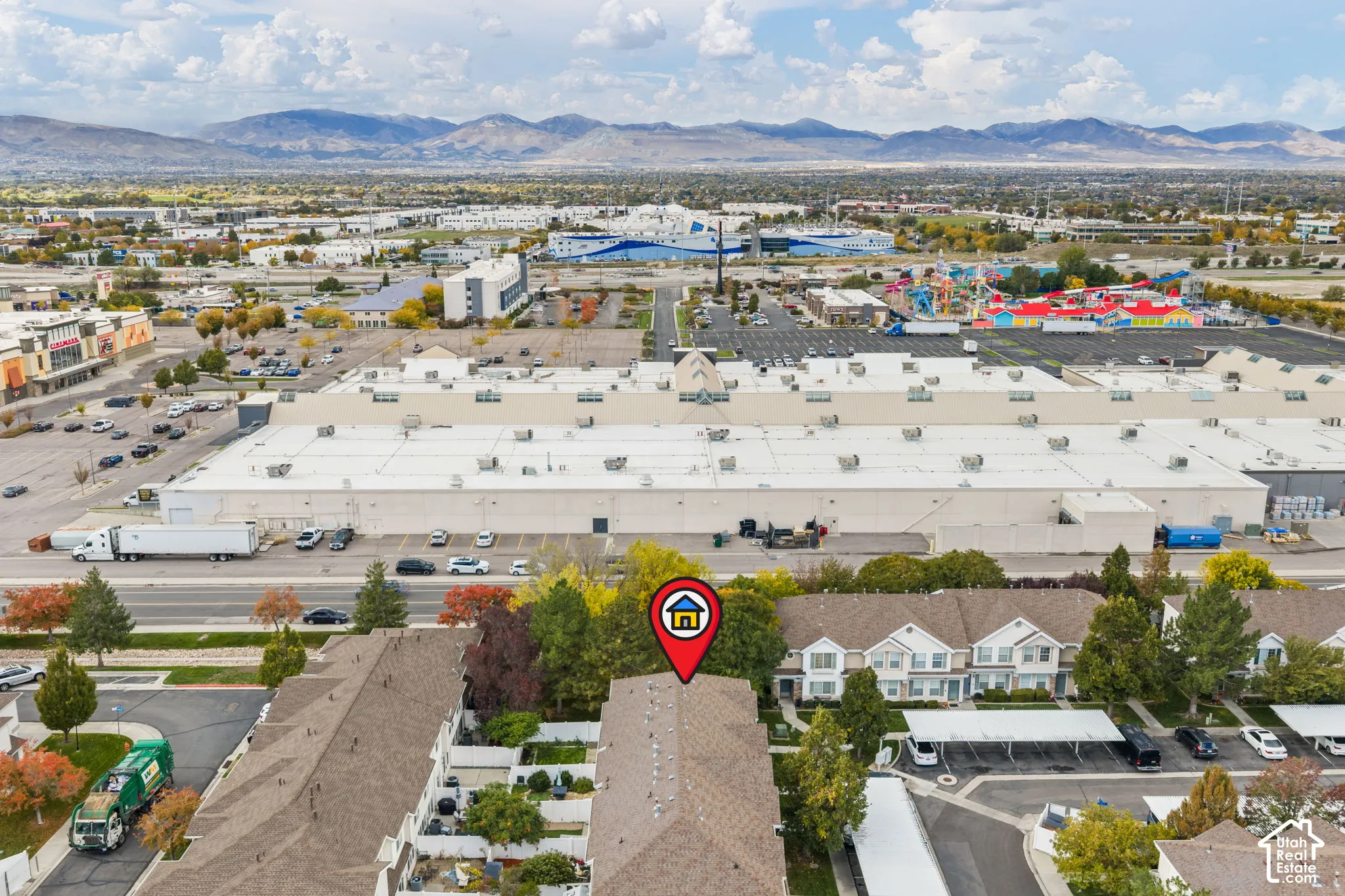 Aerial perspective of residential townhome community featuring asphalt shingle roofing, covered parking structures, mature trees, and a mountain range backdrop