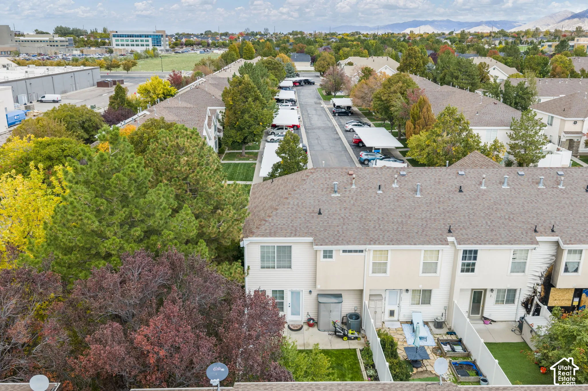 Aerial perspective of a multi-level residential structure featuring light-toned siding, shingled roofing, fenced private outdoor space, and proximity to mature trees and neighborhood green space