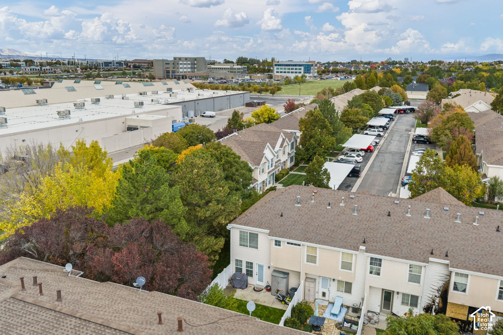 Aerial perspective featuring multi-story residential buildings, shingled roofing, paved parking areas with covered carports, and mature landscaping