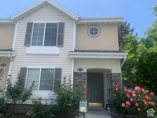 Two-story exterior featuring light-colored horizontal siding, stucco facade, stone veneer accents, decorative shutters, and a circular accent window