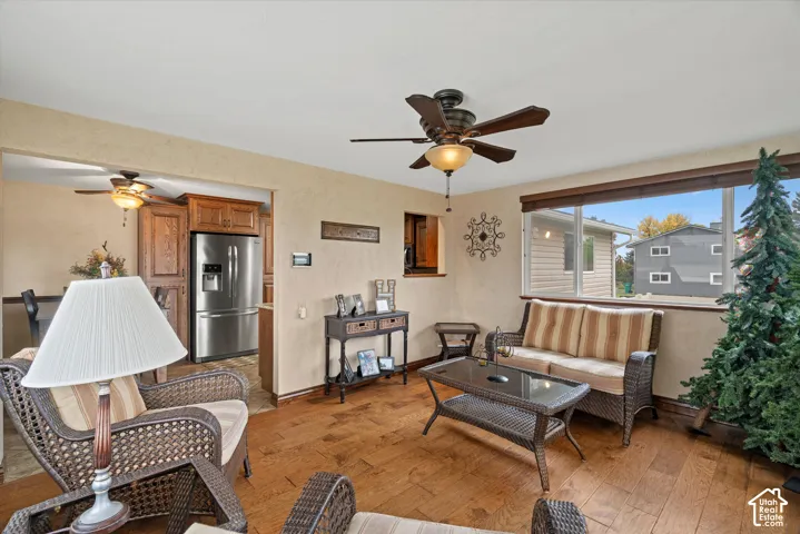 Open-concept interior featuring wood-finish flooring, a multi-blade ceiling fan with integrated lighting, and a large picture window