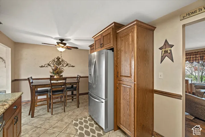 Custom wood-finish cabinetry, floor-to-ceiling pantry storage, stainless steel French-door refrigerator, tile flooring, and ceiling fan with integrated lighting