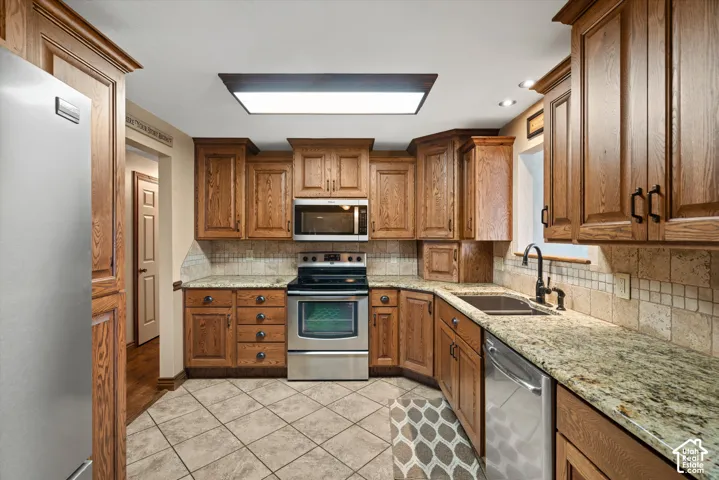 Kitchen featuring shaker-style wood cabinetry, natural stone countertops, a tiled backsplash, stainless steel appliances, and tile flooring