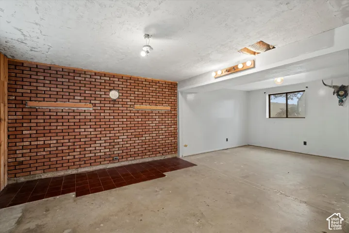 Interior space featuring an exposed red brick accent wall, tiled hearth, concrete flooring, and a window with exterior exposure