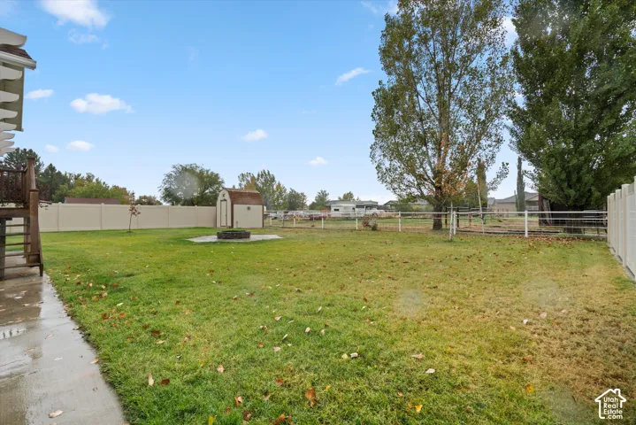 Expansive backyard featuring a manicured lawn, full-perimeter vinyl fencing, a detached storage shed, and a stone fire pit