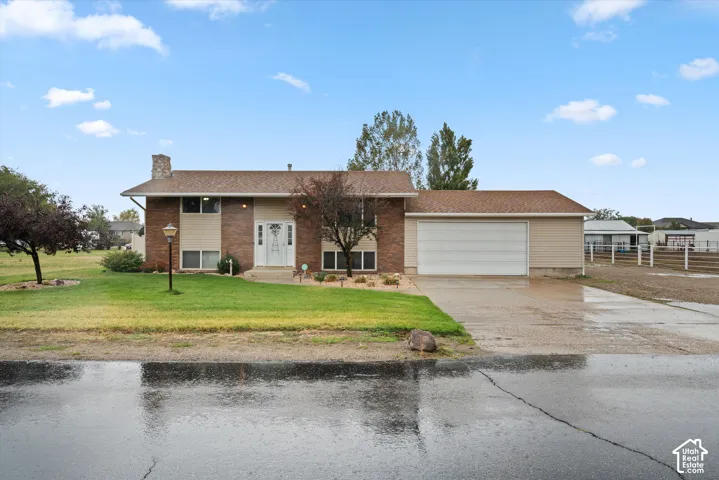 Split-level exterior featuring a brick and horizontal siding facade, stone chimney, attached garage, and paved driveway