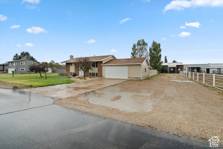 Split-level exterior featuring a brick and horizontal siding facade, two-car attached garage, paved driveway, gravel parking area, and white post-and-rail fencing