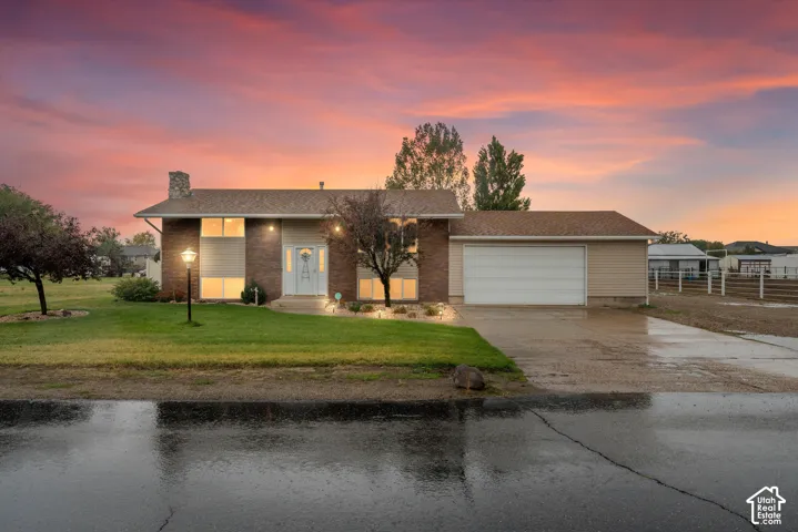 Split-level exterior featuring a brick facade, attached two-car garage, stone-finished chimney, and concrete driveway