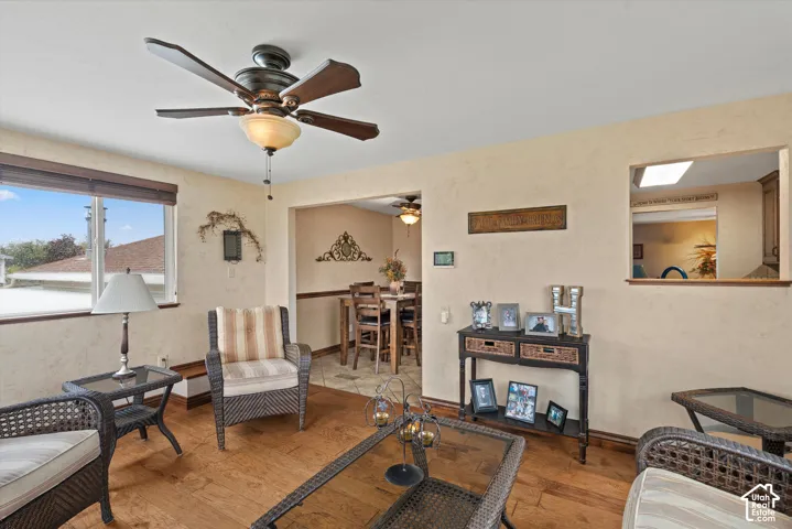 Wood-finish flooring, ceiling fan with integrated lighting, textured walls, and a pass-through opening