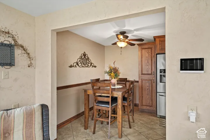 Textured walls with wooden chair rail molding, tile flooring, built-in wooden cabinetry, stainless steel refrigerator, and ceiling-mounted light fixture