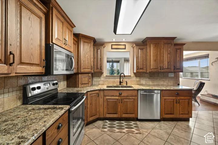 Kitchen featuring wood cabinetry, stone countertops, stone tile backsplash, stainless steel appliances, and ceramic tile flooring