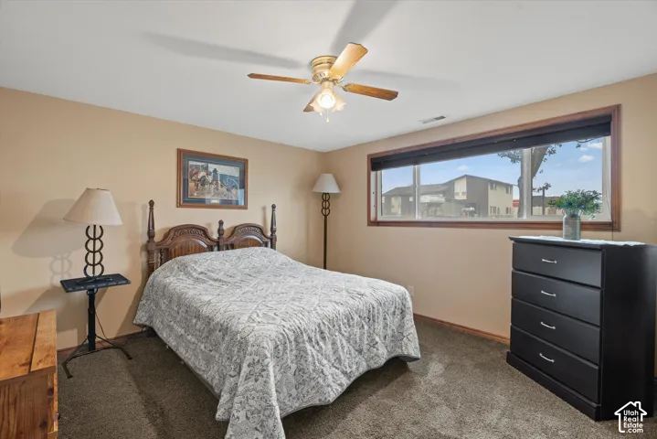 Carpeted room featuring a ceiling fan with light fixture and a wide window with wood trim