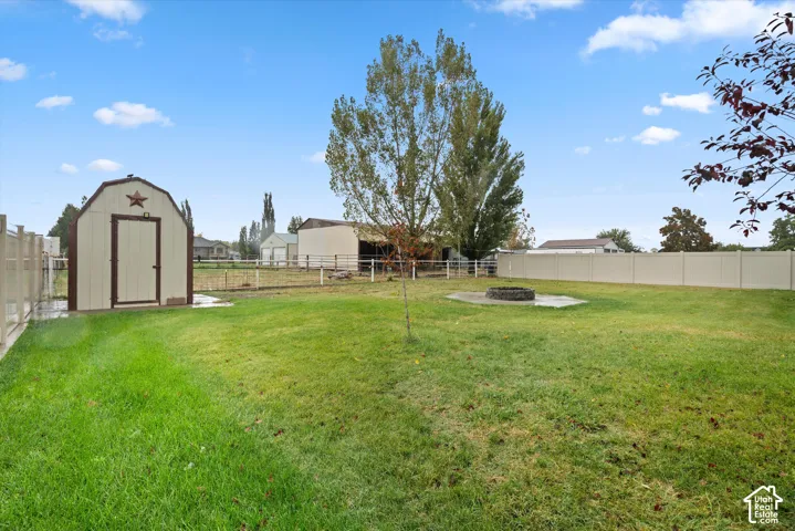 Fenced backyard featuring a manicured lawn, detached storage shed, circular stone fire pit, and mature trees