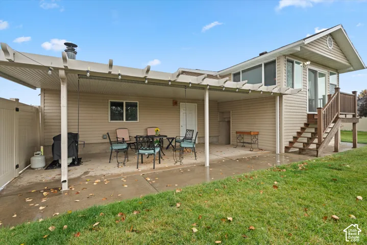 Covered concrete patio featuring a pergola structure, elevated wooden deck with stairs, vinyl siding, and white vinyl privacy fencing