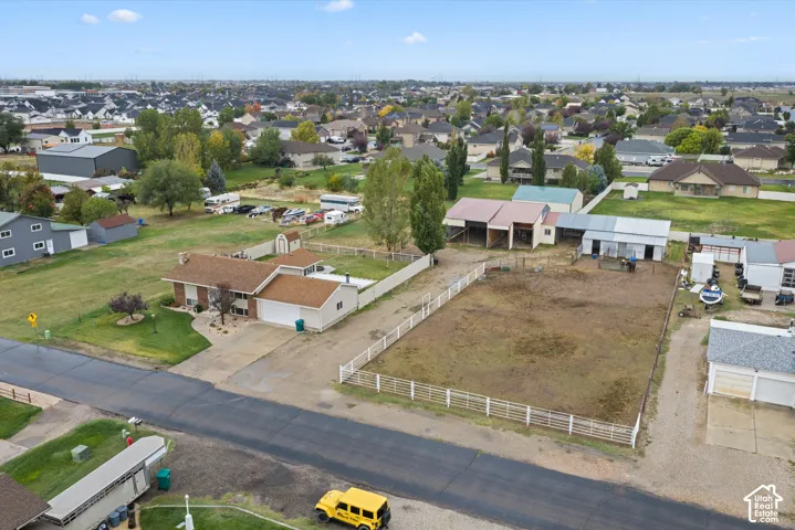 Aerial perspective of a property featuring an expansive lot, a residence with an attached garage, fenced pastures, and multi-stall outbuildings