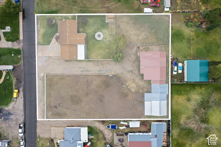 Aerial perspective of expansive lot featuring a residence with a shingled roof, a detached outbuilding with a metal roof, an open-air fire pit, and extensive acreage