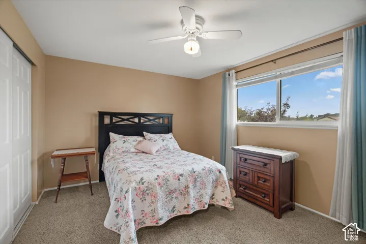 Neutral-toned walls, wall-to-wall carpeting, ceiling-mounted light fixture with fan, wide window, and sliding-door closet