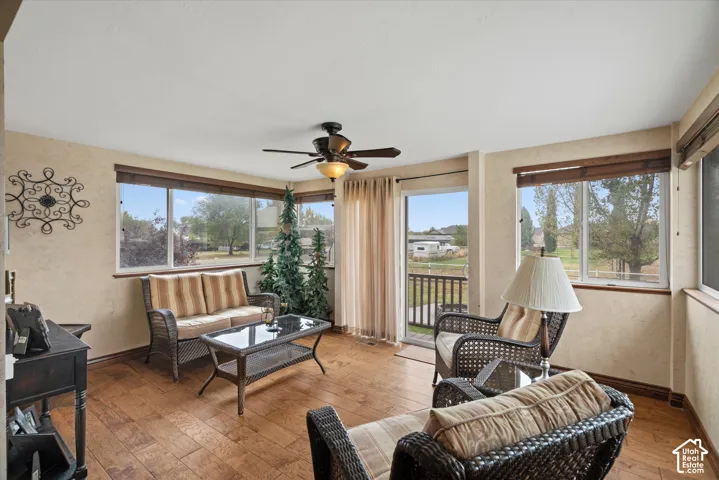 Sunroom featuring wood-finish flooring, extensive windows, a ceiling fan with integrated lighting, and a glass-paneled exterior door