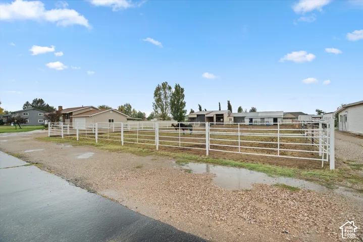 Expansive outdoor area featuring white tubular steel fencing, multiple auxiliary structures, gravel surfacing, and open-ground paddocks