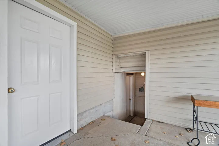 Covered exterior entrance featuring horizontal lap siding, a six-panel door, concrete porch flooring, and an integrated stairwell entry
