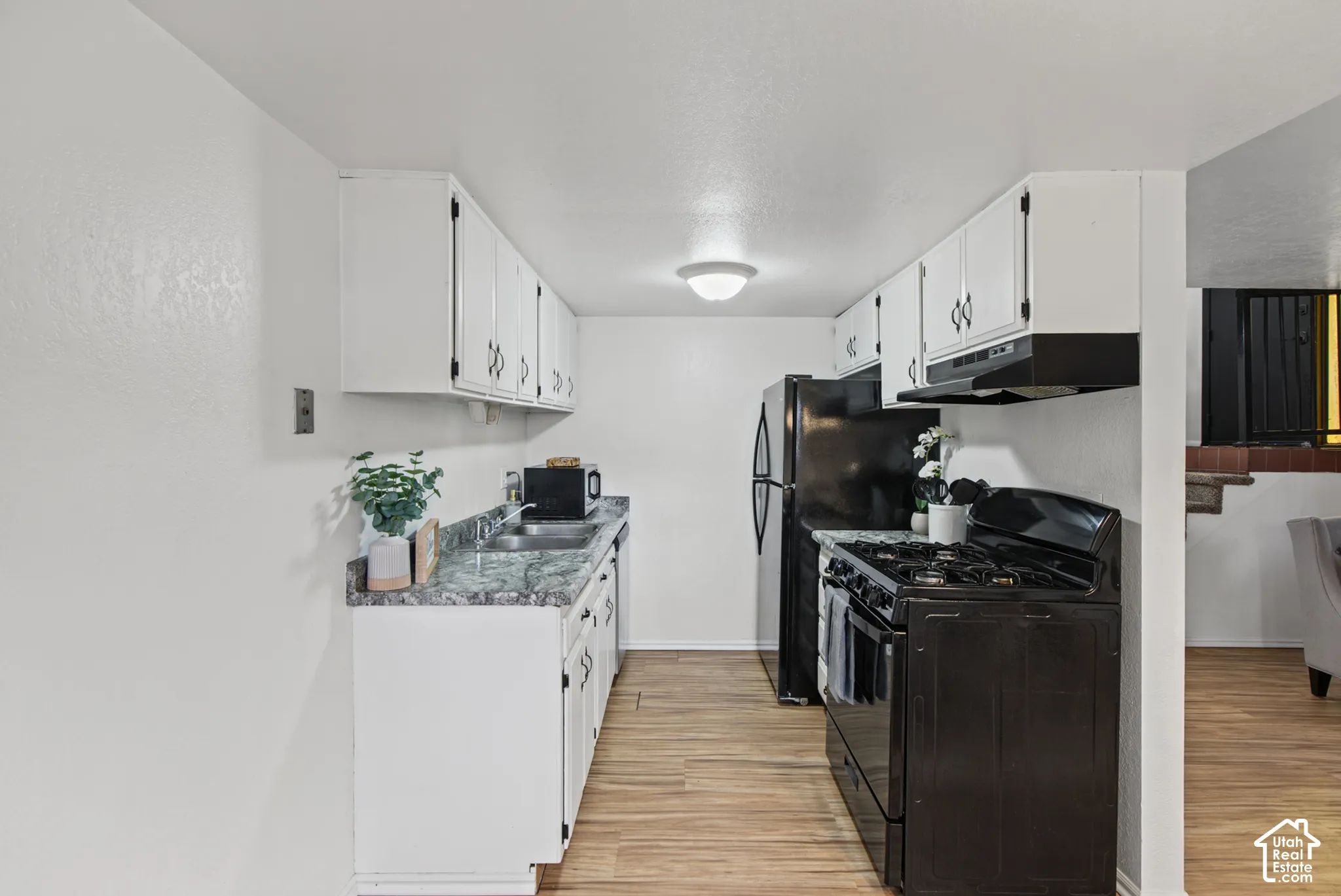 Kitchen featuring white cabinetry, patterned stone-finish countertops, wood-finish flooring, and black appliances including a gas range