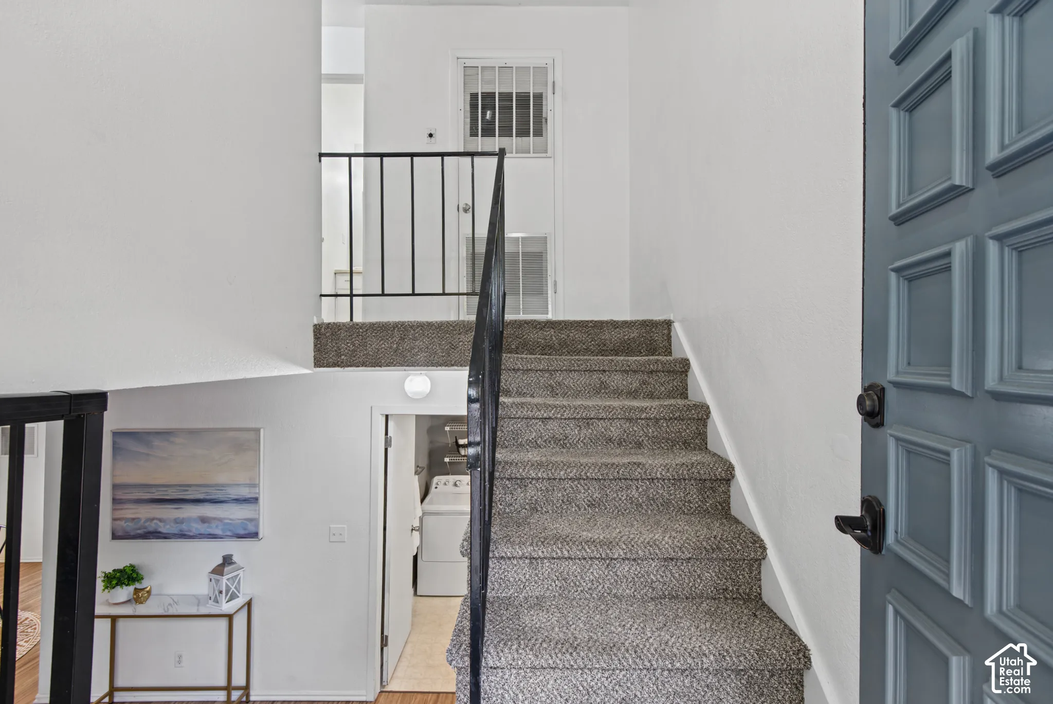 Entryway featuring a multi-panel door with matte black hardware, carpeted staircase, and a metal handrail