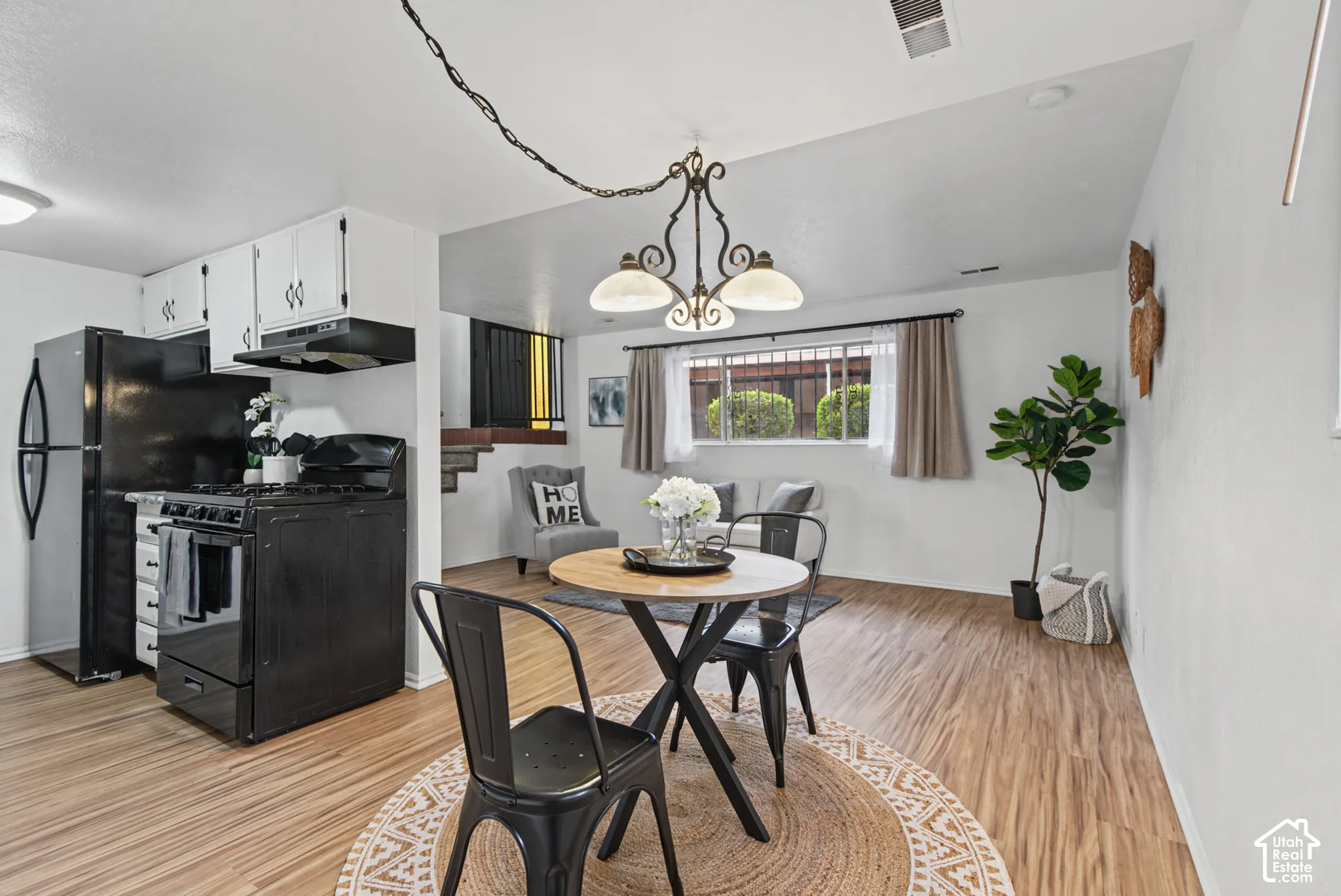 Kitchen featuring white cabinetry, black appliances, wood-finish flooring, and a decorative multi-arm chandelier