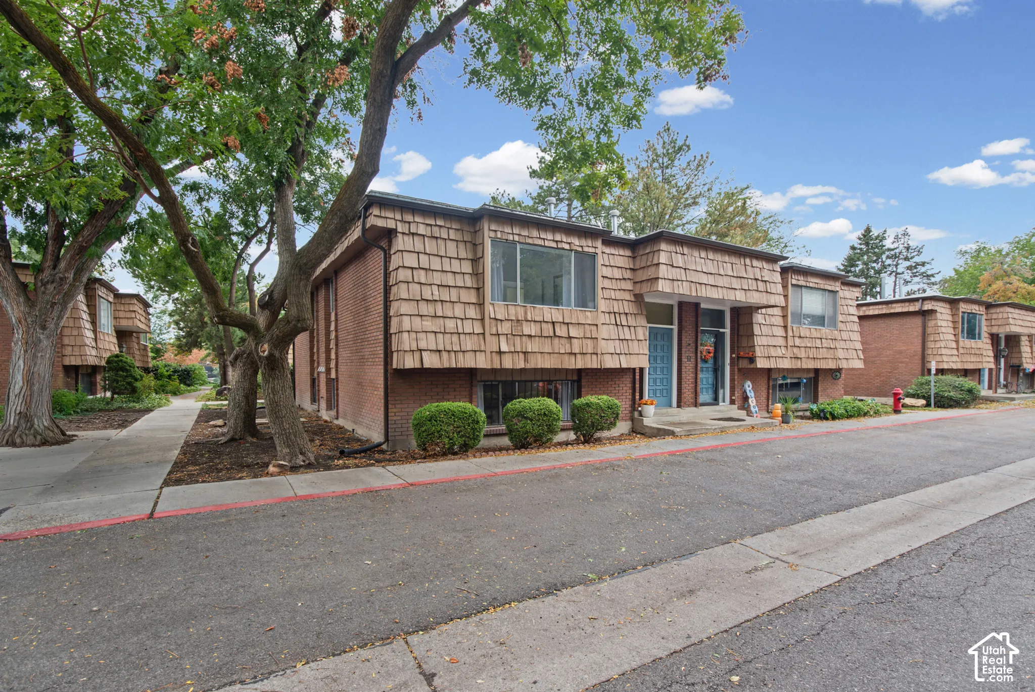 Exterior facade featuring a combination of brick masonry and wood-shake siding, shingled overhangs, and mature shade trees