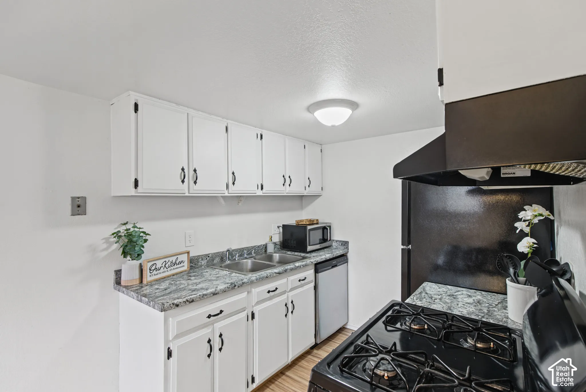 Kitchen featuring white cabinetry with black hardware, patterned laminate countertops, a double-basin stainless steel sink, and a black gas range