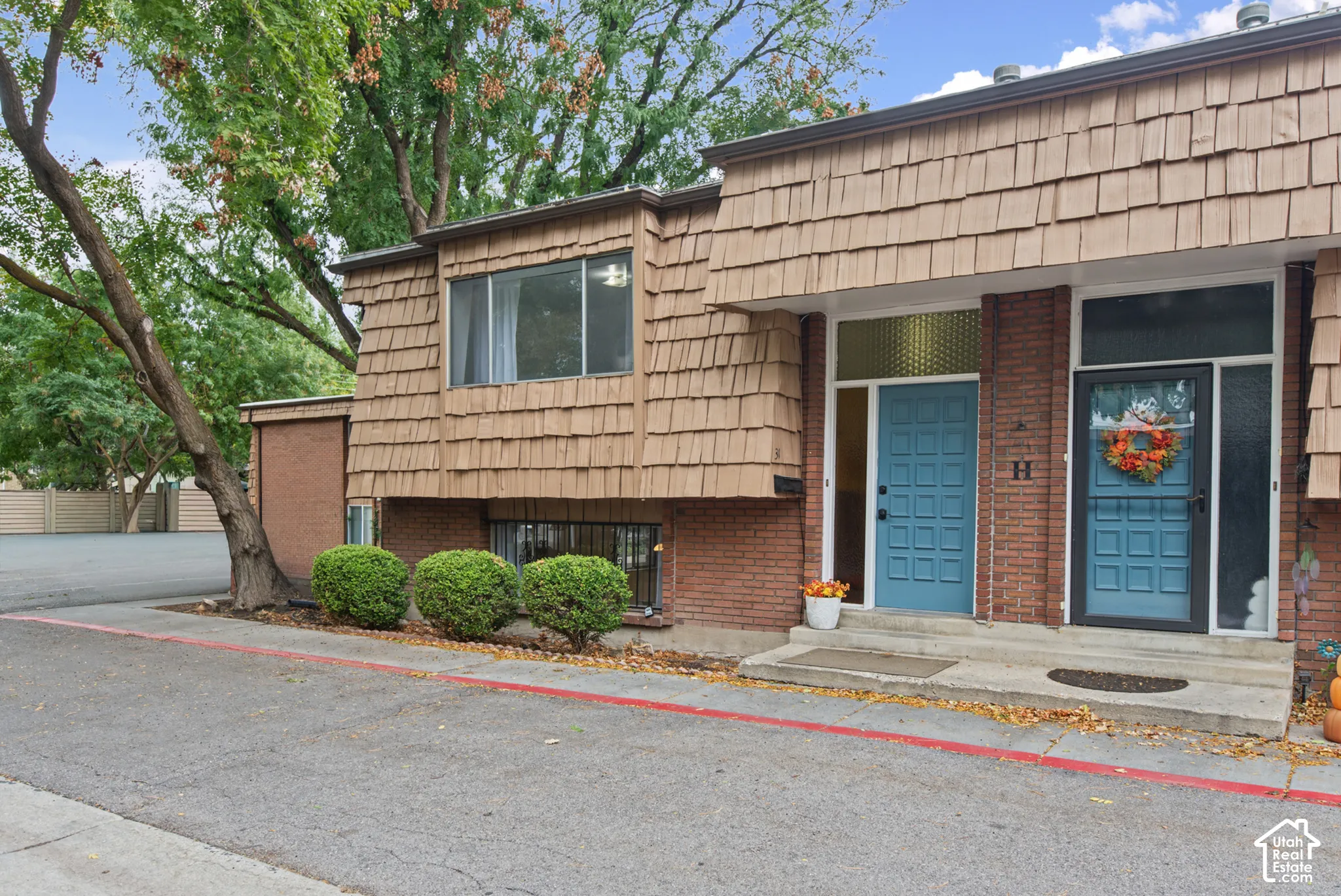 Exterior facade featuring a combination of red brick masonry and wood-shake siding, dual front entry doors with inset panel detailing, and multi-paned windows