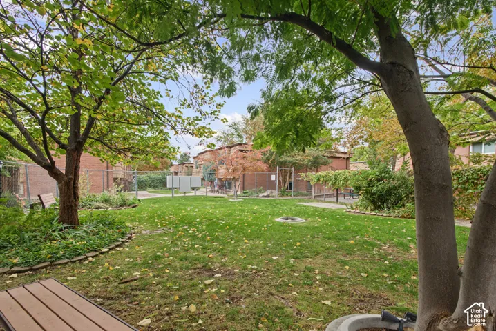 Shared outdoor courtyard featuring a grass lawn, mature trees, brick exterior construction, and chain-link perimeter fencing