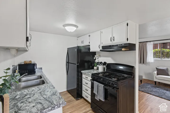 Kitchen featuring white cabinetry, stone-patterned laminate countertops, dual-basin stainless steel sink, black appliance suite, and wood-finish flooring