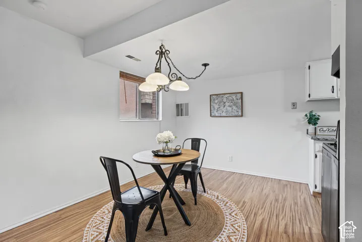 Dining area featuring wood-finish flooring, a multi-arm scrolled metal chandelier, and white cabinetry
