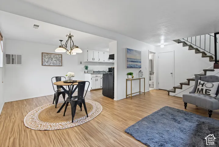 Wood-finish flooring, white cabinetry, iron-style chandelier, and carpeted staircase with an iron railing