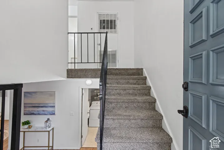 Entryway featuring a multi-panel door with matte black hardware, carpeted staircase, and a metal handrail