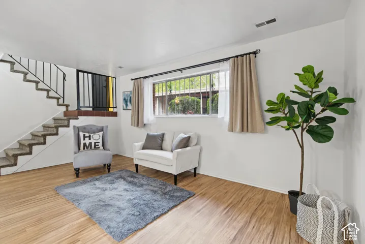 Living area featuring wood-finish flooring, a large window with metal security bars, and an architectural staircase with a wrought-iron railing