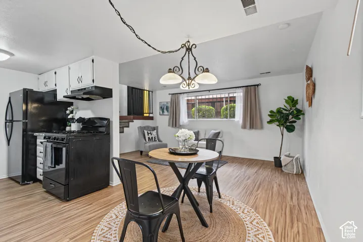 Kitchen featuring white cabinetry, black appliances, wood-finish flooring, and a decorative multi-arm chandelier