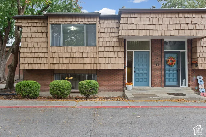 Exterior facade featuring brick masonry and shingle-style siding, topped with a mansard roofline, complemented by paneled entry doors and rectangular windows with transom accents
