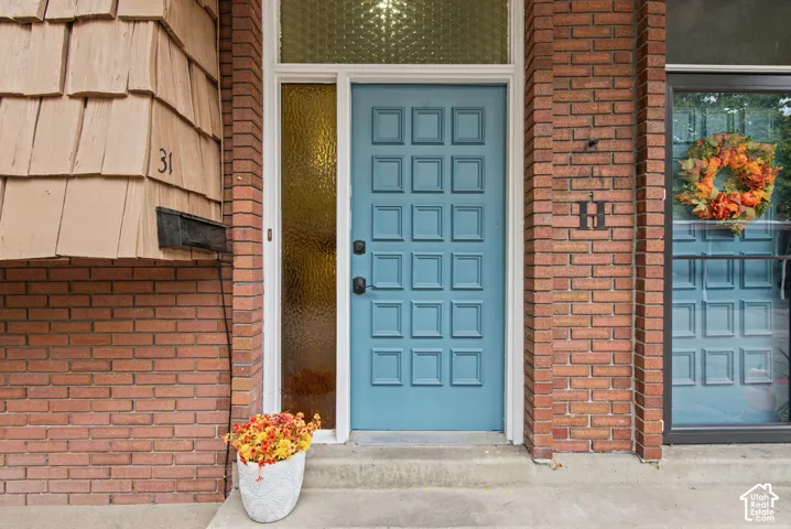 Exterior entrance featuring a red brick facade, wood-shingle accenting, a panelled blue door, and textured glass sidelights and transom windows