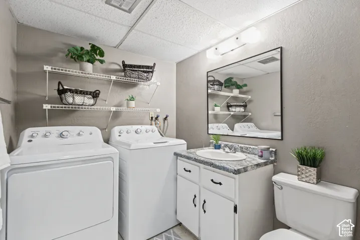 Laundry area featuring dual white wire shelving, a vanity with a patterned countertop, an integrated oval sink, and a rectangular mirror with a three-bulb light fixture