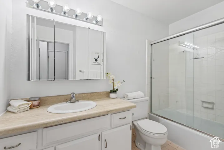 Bathroom featuring a white vanity with a neutral-toned countertop, integrated oval basin, tri-fold mirrored medicine cabinet, six-bulb overhead light fixture, and a glass-enclosed shower and tub combination