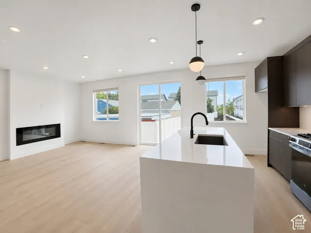 Kitchen featuring an oversized island with a solid-surface countertop, linear built-in fireplace, recessed lighting, modern pendant fixtures, and wood-finish flooring