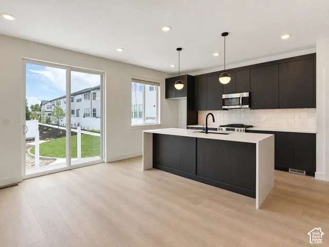 Kitchen featuring flat-panel dark cabinetry, quartz waterfall island with undermount sink, matte black fixtures, recessed lighting, and wood-finish flooring