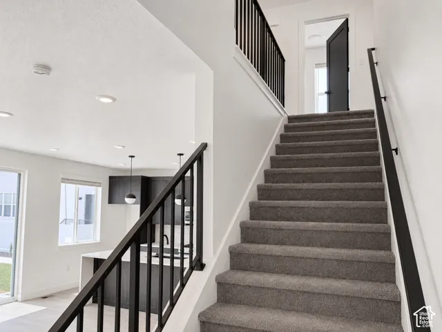 Staircase featuring charcoal carpeted treads, a matte black metal railing, recessed ceiling lighting, and a neutral color palette