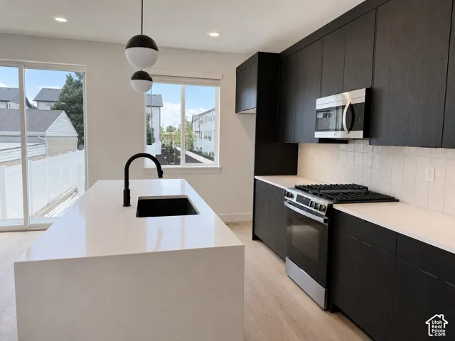 Kitchen featuring flat-panel dark cabinetry, quartz countertops, a central island with a matte black faucet, stainless steel gas range, and square tile backsplash